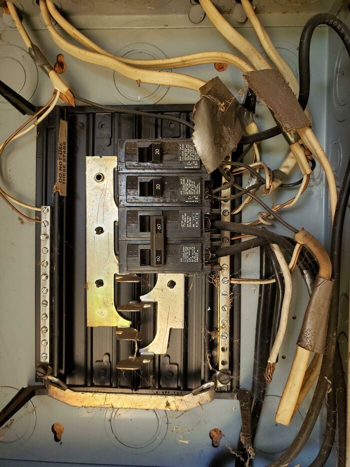 Old electrical panel with exposed wiring and damaged insulation, illustrating home safety issues people regretted after buying.