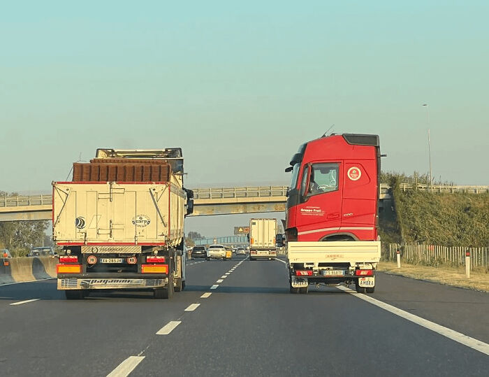 Two trucks on a highway with one red cab oddly placed on a smaller flatbed, part of unedited photos that mess with your brain.