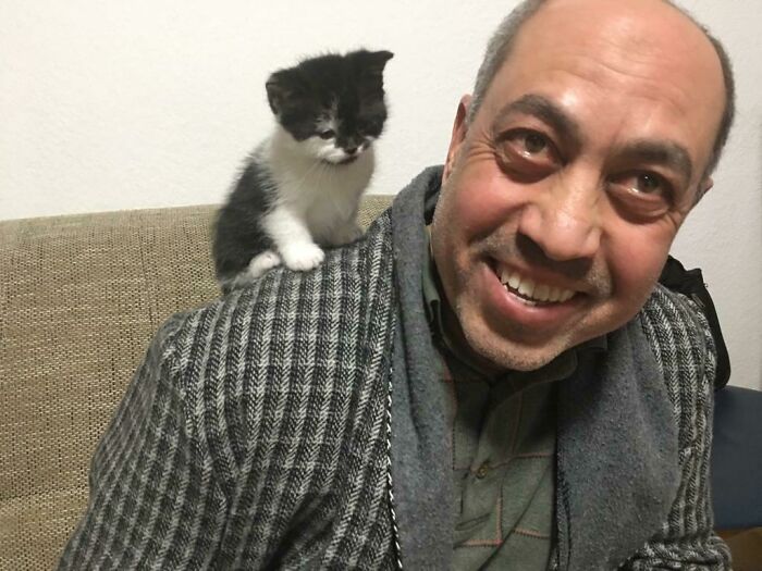 Man smiling with a small black and white kitten on his shoulder, showing dads and the pets they never wanted but love