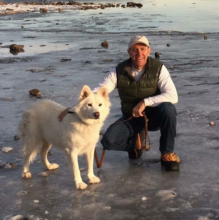 Man kneeling beside a white dog on a frozen lake, showcasing dads and the pets they never wanted but now love.