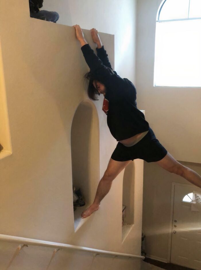 Man hanging on ledge inside home with cat nearby, illustrating unexpected moments between dads and the pets they never wanted.