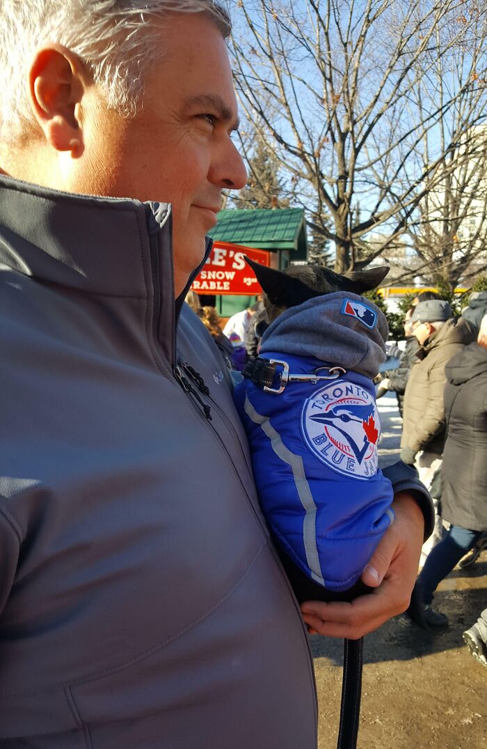 Man holding small dog wearing a Toronto Blue Jays jacket, showcasing dads and pets bond in an outdoor winter setting.