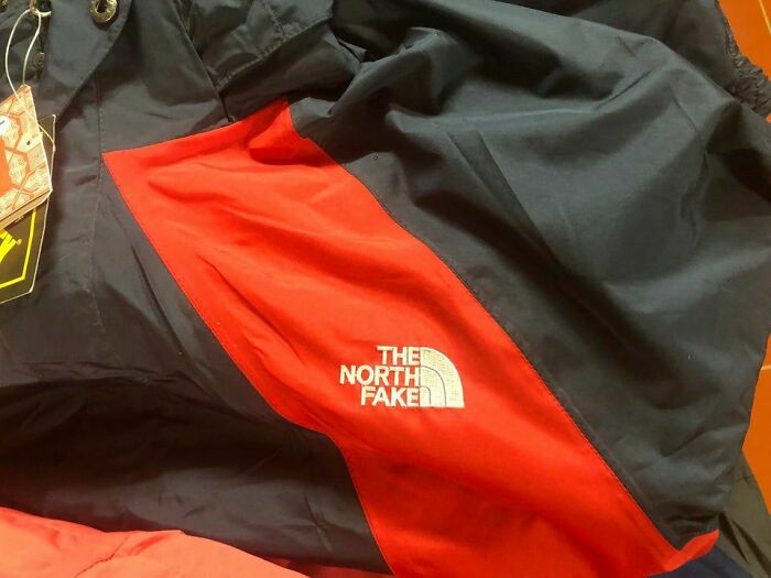 Jacket with shameless designer copy of famous brand The North Face labeled The North Fake on red and black fabric.