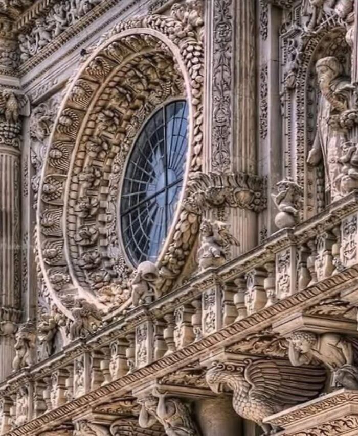 Intricate detailed carvings and sculptures surround a large circular window on a strange earth architectural facade.