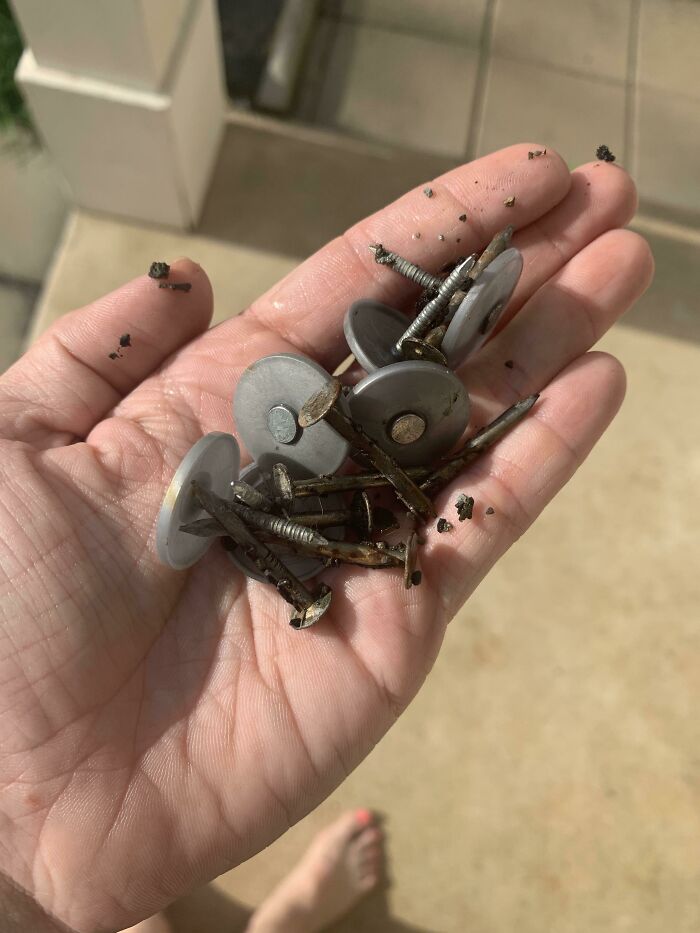 Hand holding rusted nails and washers on a concrete floor, illustrating home repairs and buying homes regrets.