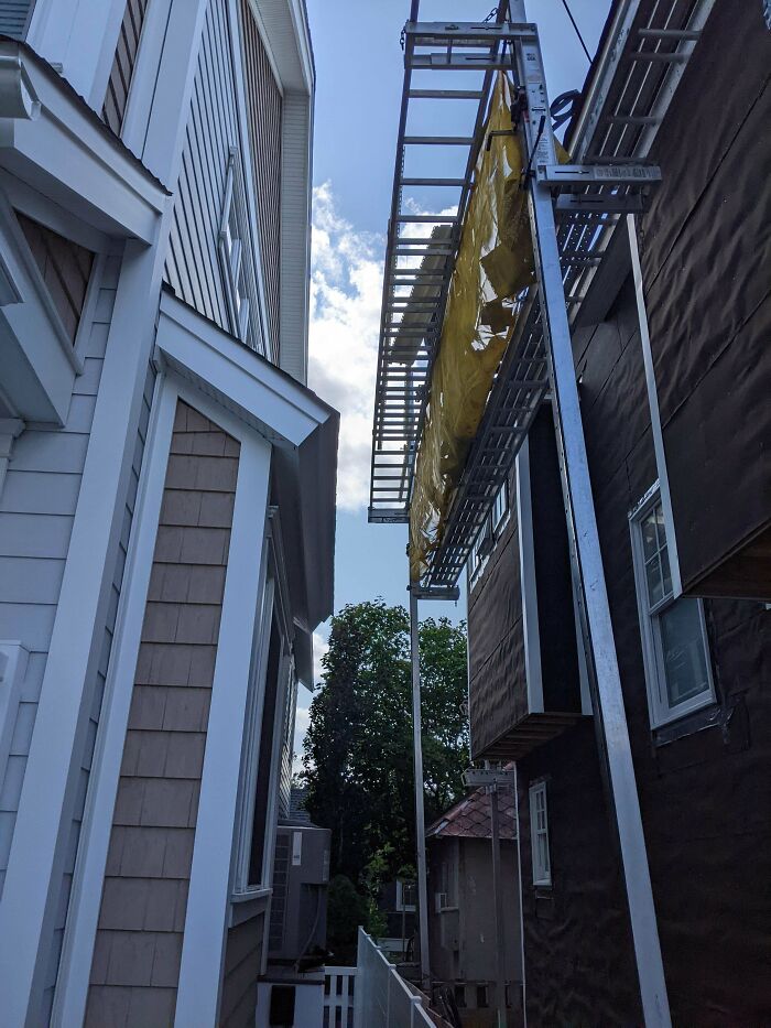Narrow gap between houses with construction scaffolding and limited outdoor space in a neighborhood setting.