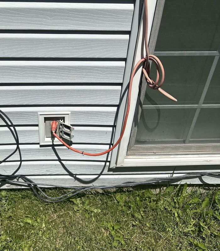 Outdoor electrical outlet with a tangled extension cord on house siding near a window in a remote neighbor setting