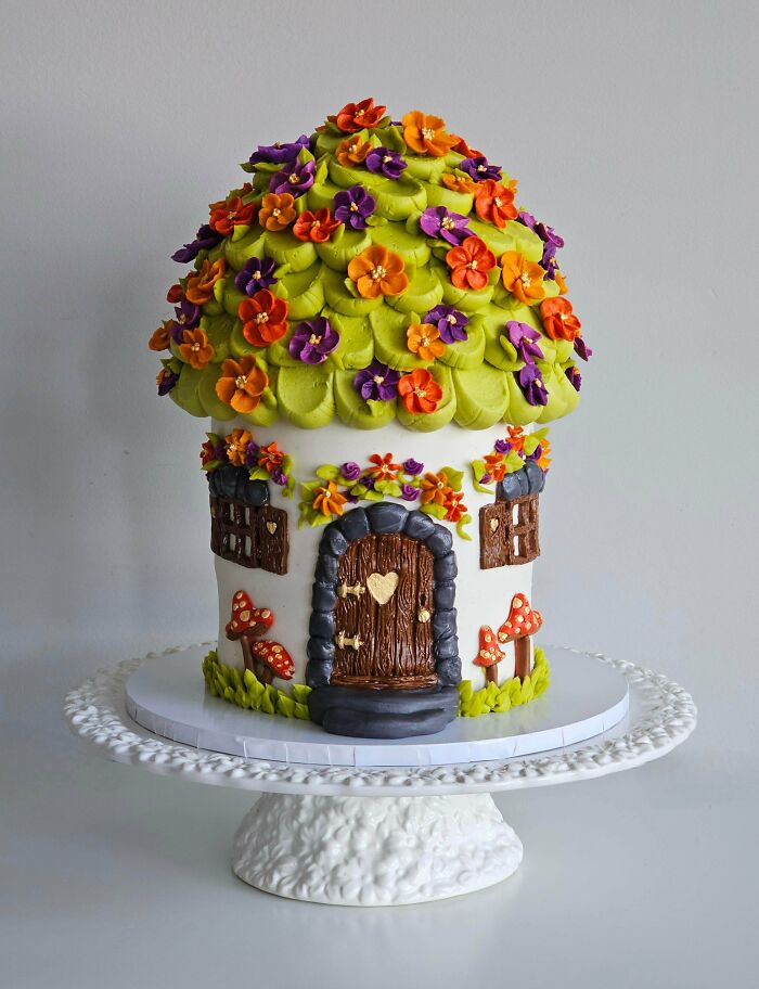 Fairy tale house cake decorated with green frosting and colorful edible flowers