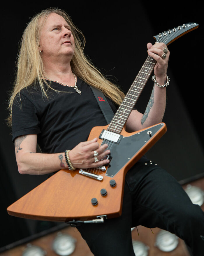Jerry Cantrell playing a guitar on stage, wearing a black shirt, showcasing his bio and career highlights in music.