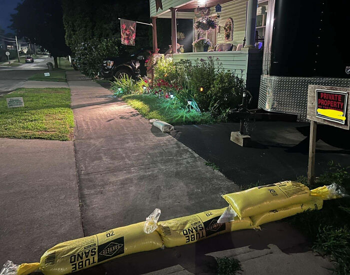 Concrete barrier made of sandbags blocking driveway in a residential area with a private property sign at night.
