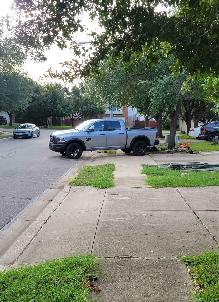 Pickup truck parked halfway on a sidewalk and grass patch in a suburban neighborhood showing unusual neighbor parking behavior.
