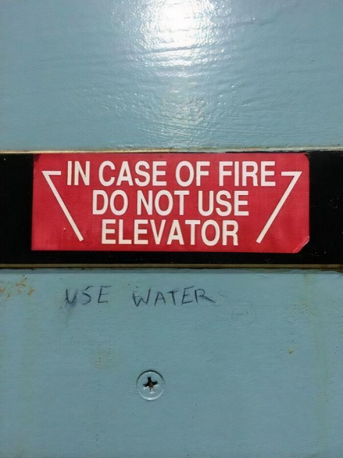 Mild vandalism shows a fire safety sign with added graffiti saying Use Water on a light blue metal surface.