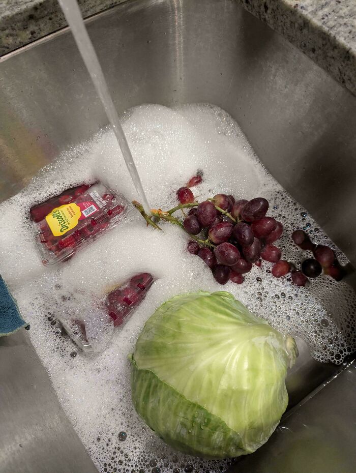 Unexplainable image of grapes and cabbage submerged in soapy water running in a kitchen sink.