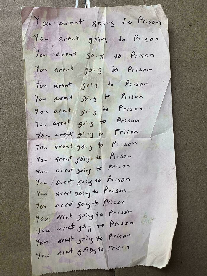 A worn, stained piece of paper repeatedly handwritten with the phrase you arent going to prison in uneven text.