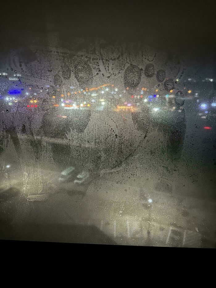 Fogged window with strange handprints and a blurred cityscape with colorful lights at night in a weird unexplainable image.