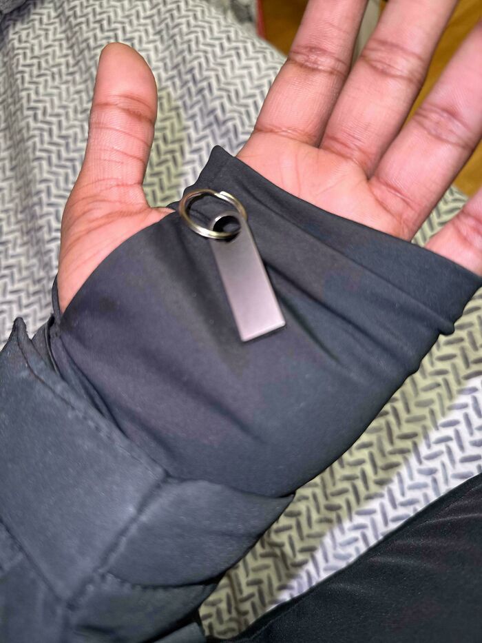 Hand wearing black sleeve with a keychain ring stuck between thumb and index finger - weird and unexplainable image.