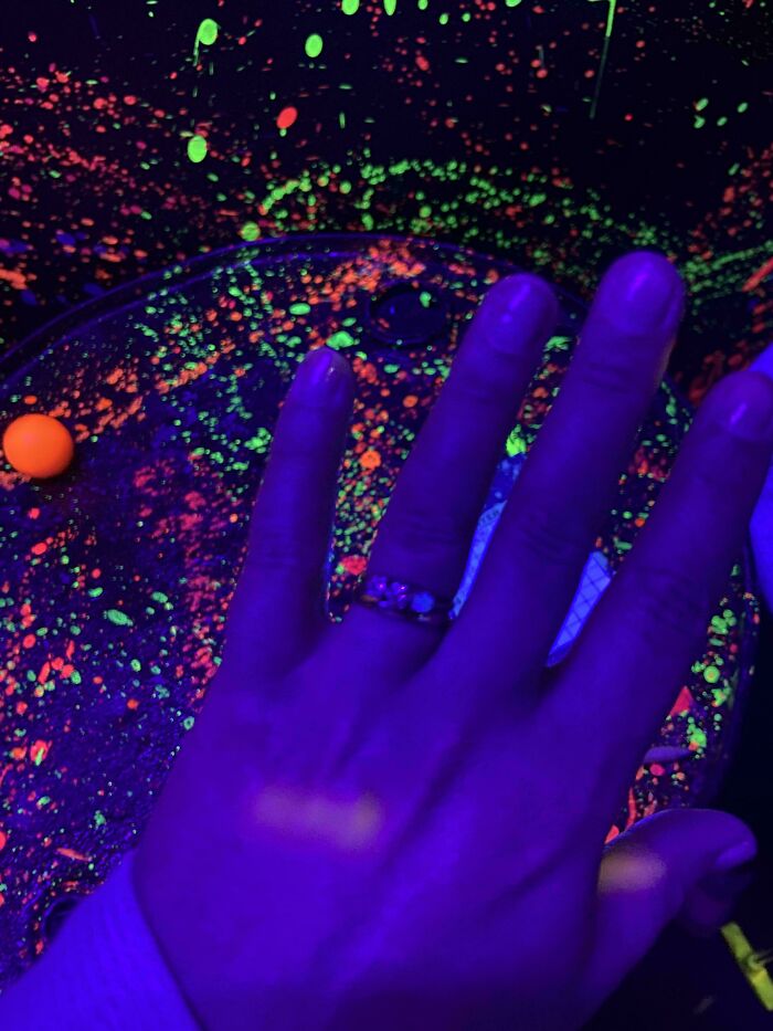 Hand under blacklight showing a glowing ring and bright neon paint splatters in weird unexplainable image.