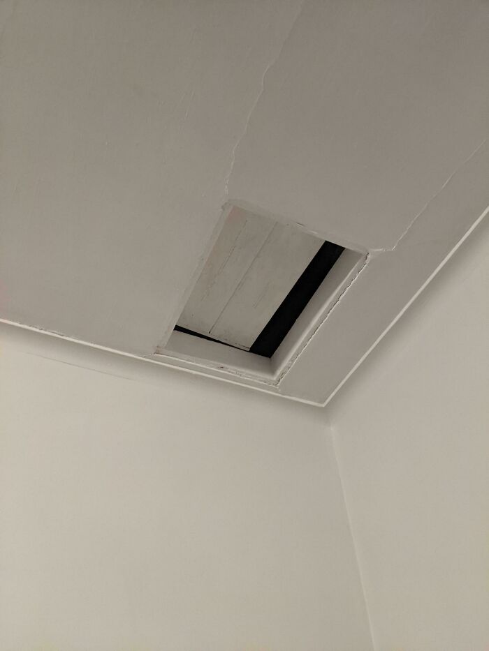 Unexplainable image of a mysterious ceiling opening with cracked edges in a plain white room corner.