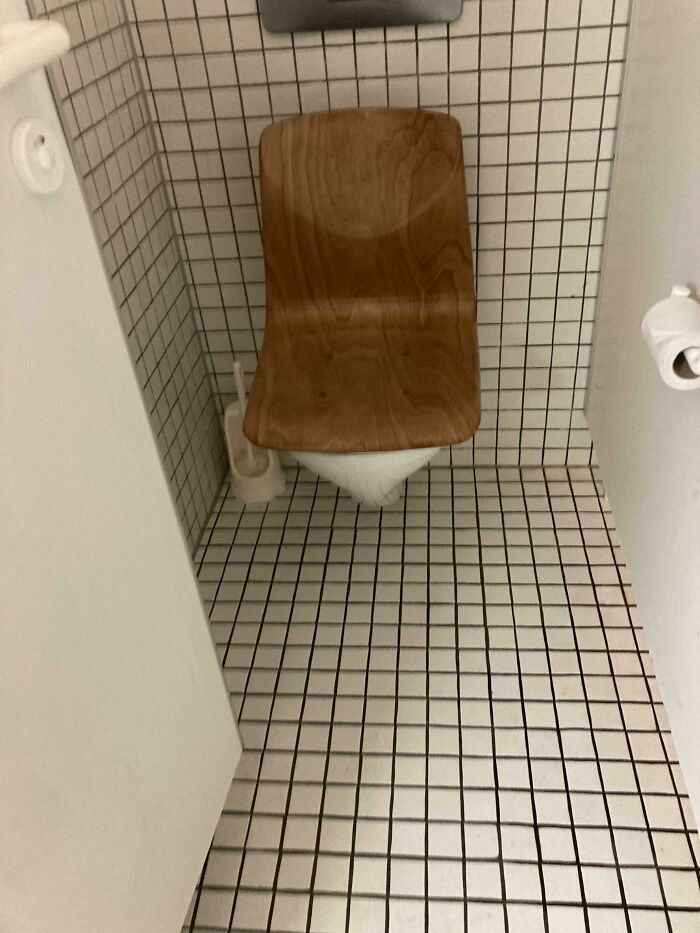 Wooden chair seemingly floating above tiled toilet in a small bathroom, a weird and unexplainable image.