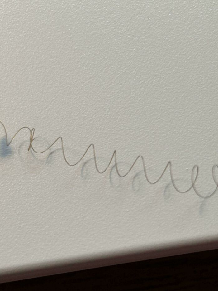 Thin curly wire segment casting a detailed shadow on a textured white surface in a weird unexplainable image.