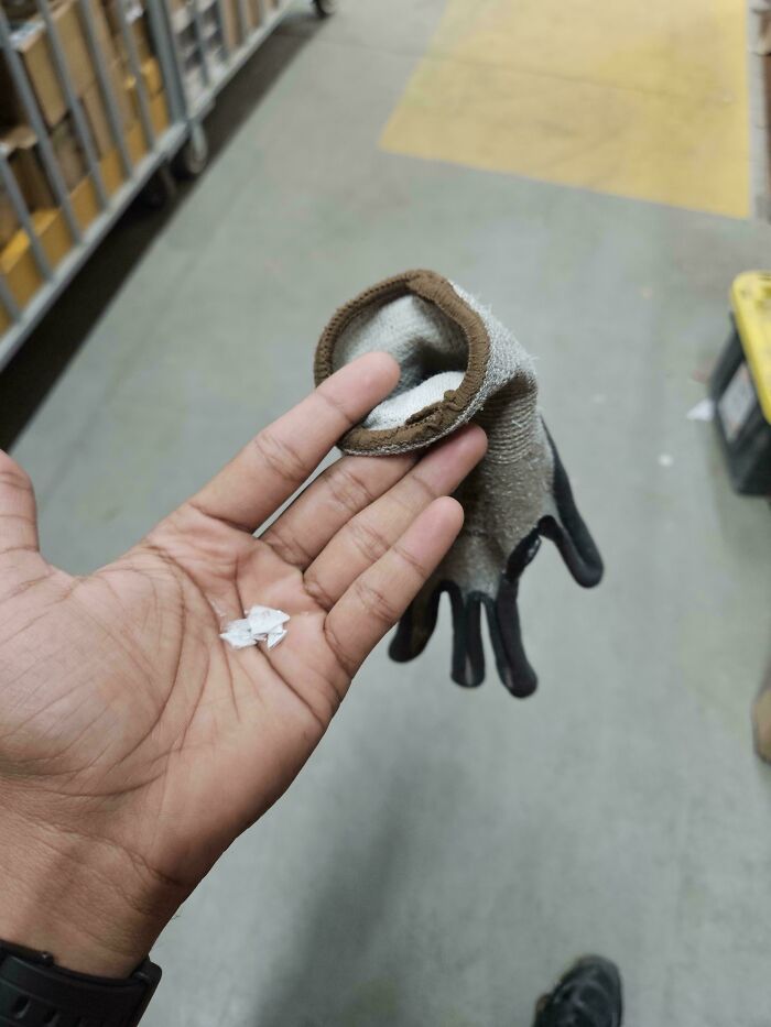 Hand holding torn glove and small pieces of white debris in an indoor industrial setting, a weird and unexplainable image.