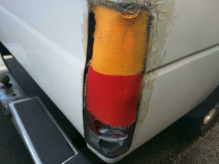 Rear taillight on a white truck patched with red and yellow tape showing redneck engineering repair.