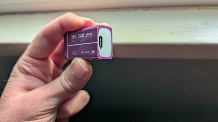 A hand holding a 9V battery with a Micro USB port, an unusual and funny job fail for a battery.