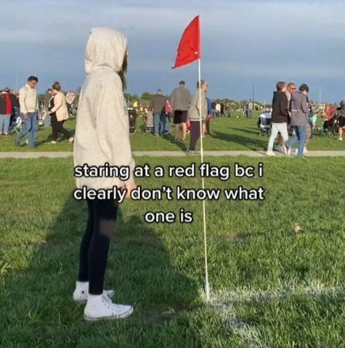 Person in a hoodie looking confused at a red flag on a field, humorous meme for entertaining meme lovers online.