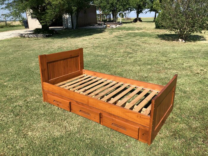 Wooden bed frame with storage drawers placed on a grass field, an unedited photo that might mess with your tired brain