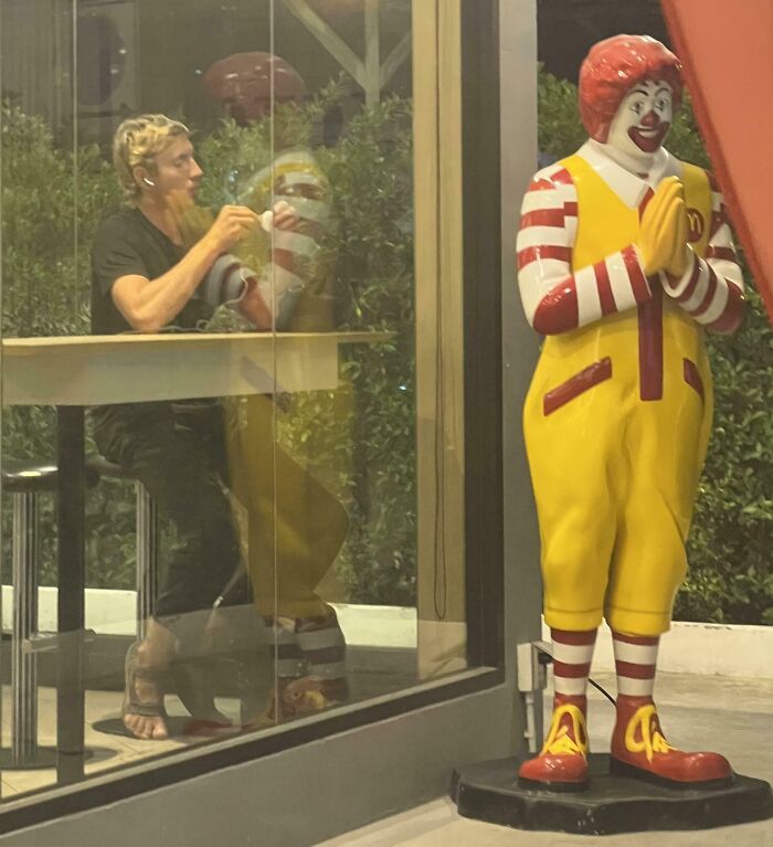 Man eating at a fast-food restaurant with a reflective glass creating a confusing visual effect messing with your brain.