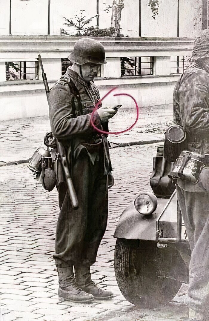 Old photograph of soldier holding a device resembling a modern smartphone, hinting at time travel theories.