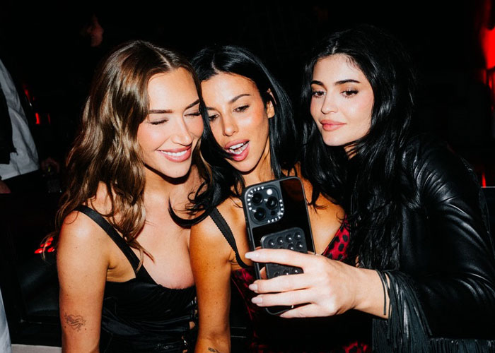 Três mulheres, incluindo Kylie Jenner, tirando uma selfie juntas em um ambiente de festa mal iluminado e com smartphones visíveis. Três mulheres, incluindo Kylie Jenner, tirando uma selfie juntas em um ambiente de festa mal iluminado e com smartphones visíveis.