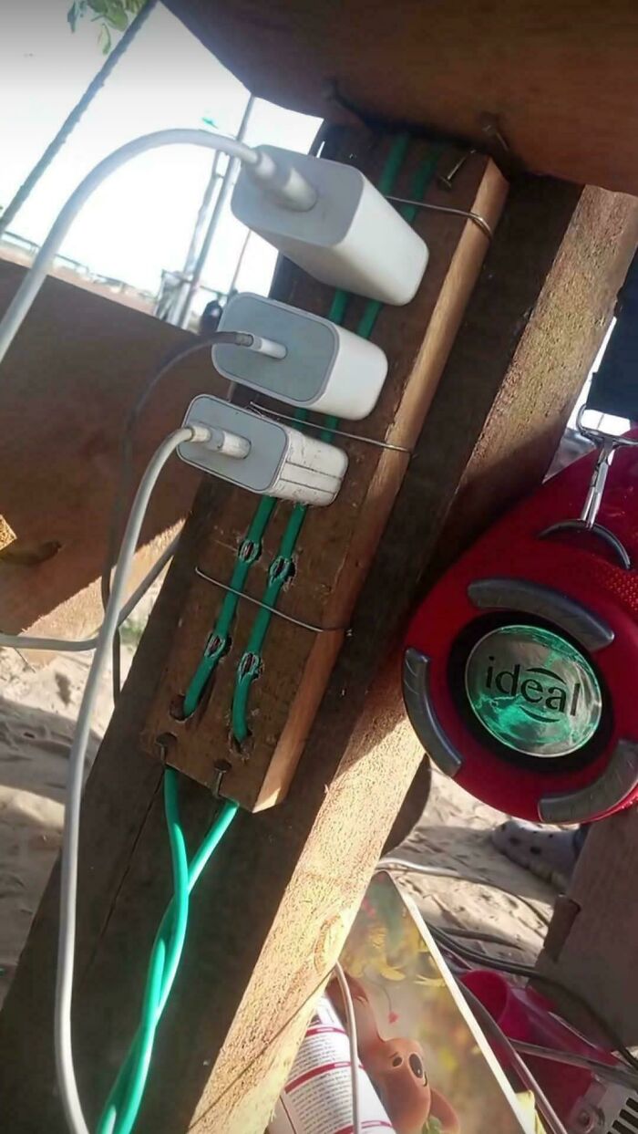 Multiple charging adapters wired into a wooden board with cords held by metal clips in an example of redneck engineering.