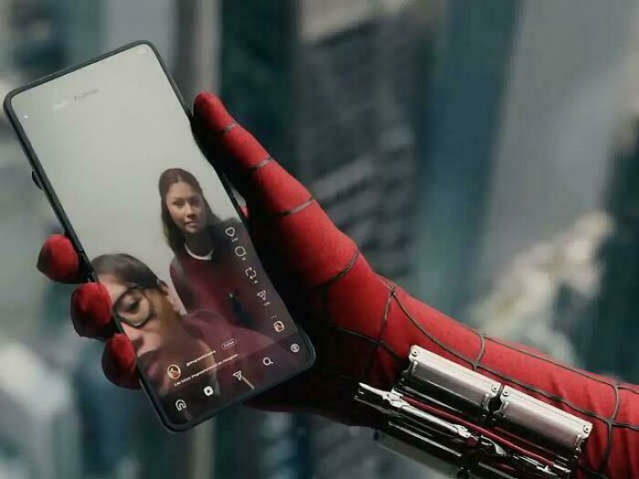 Spider-Man in his suit holding a phone displaying two women, highlighting nonsensical movie details.