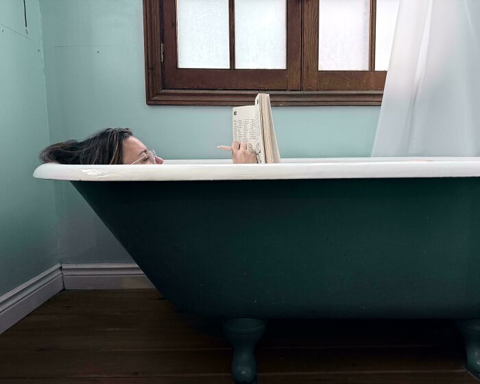 Woman relaxing and reading a book in a green clawfoot bathtub, showcasing Accidental Renaissance