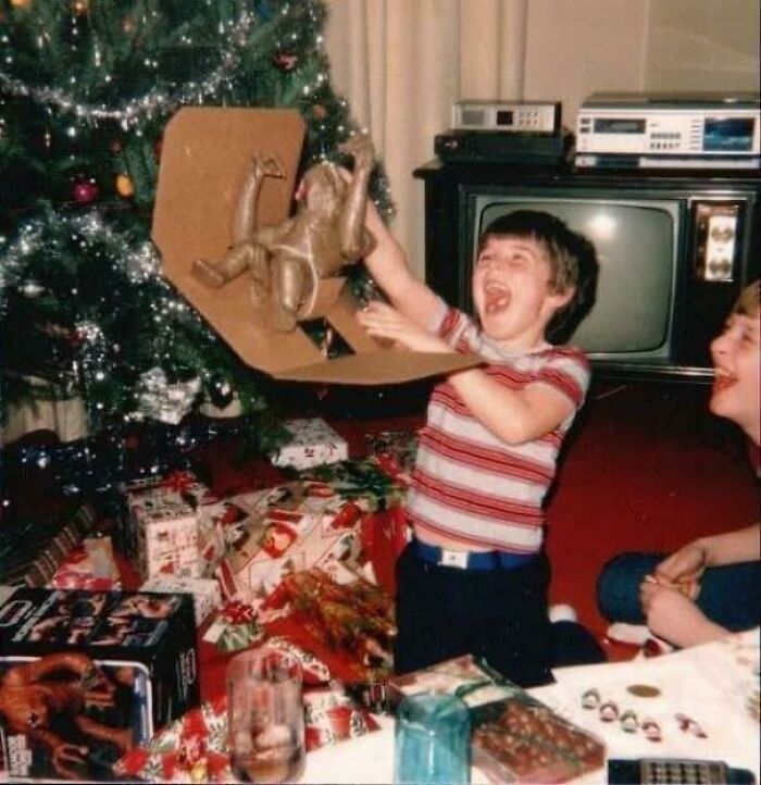 A candid old photo of a young boy excitedly unwrapping a toy gorilla next to a Christmas tree, revealing what the world looked like generations ago.