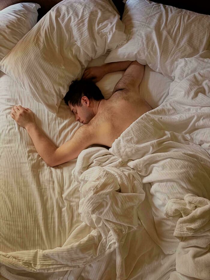 Man sleeping peacefully in a bed with tangled white sheets in an Accidental Renaissance pose
