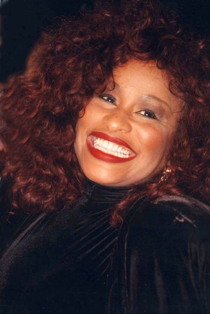 Chaka Khan smiling with voluminous curly hair and red lipstick, highlighting her iconic music career.