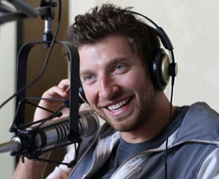 Brett Eldredge smiling while wearing headphones and speaking into a microphone during a radio show recording session