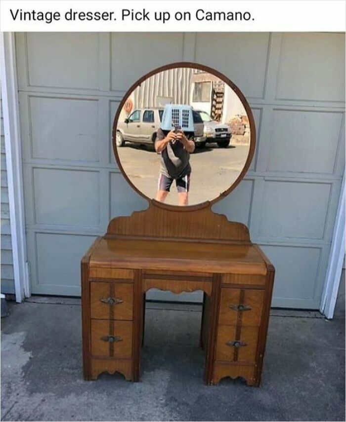Vintage dresser with a round mirror reflecting a person holding an air conditioner unit on their head on Facebook Marketplace post.