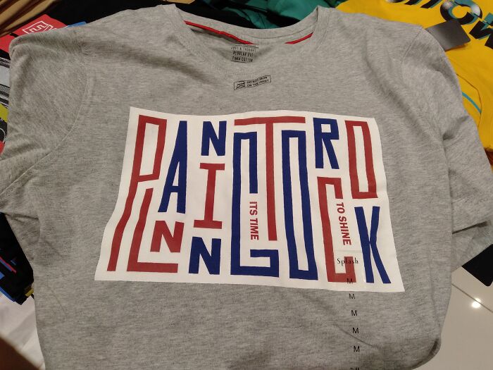 Gray t-shirt with a confusing and hilariously bad design spelling out words in red and blue block letters.