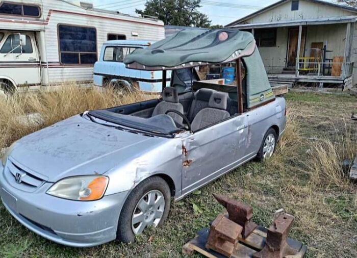 Silver convertible car with a crocodile head roof attachment parked in a yard among old vehicles, unhinged Facebook Marketplace listing.