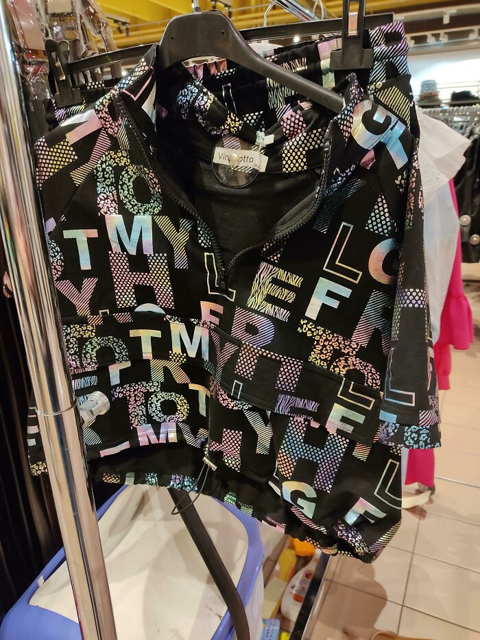 Black hoodie with a colorful random letter pattern, showcasing hilariously bad t-shirt design flaws in a retail store setting.