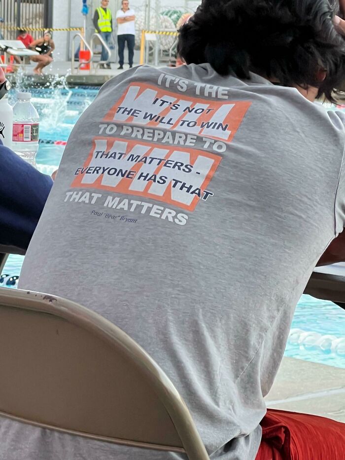 Person wearing a gray t-shirt with confusing motivational text sitting by a pool in a casual setting, showcasing bad t-shirt designs.