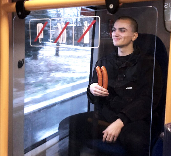 Young first-world anarchist on public transport holding two sausages, smirking defiantly and challenging social norms.