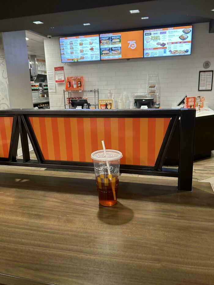 Empty fast food counter with orange striped divider and a clear cup of iced tea with a straw on the table inside restaurant interior.