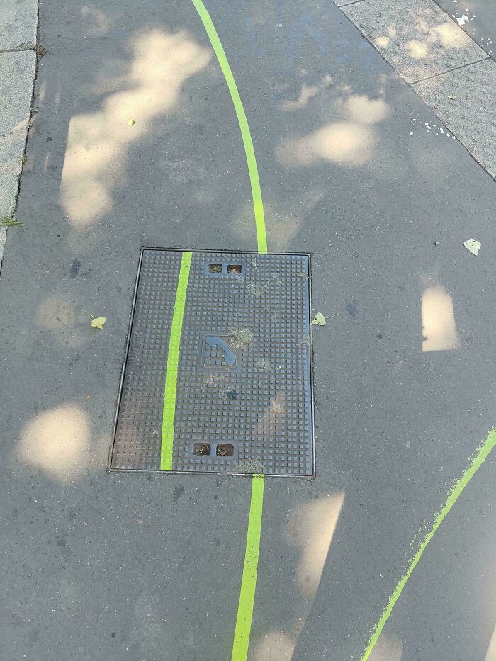 Green line painted across sidewalk and metal manhole cover, illustrating ungovernable urban street art concept.
