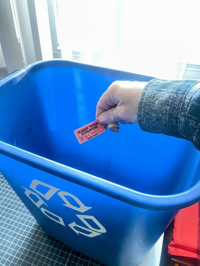 Hand holding a keep this coupon ticket above a blue recycling bin symbolizing ungovernable first-world anarchists.