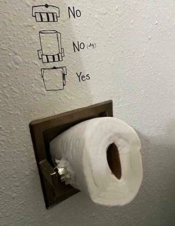 Toilet paper roll installed sideways with wall instructions, showcasing ungovernable humor in everyday first-world anarchist style.