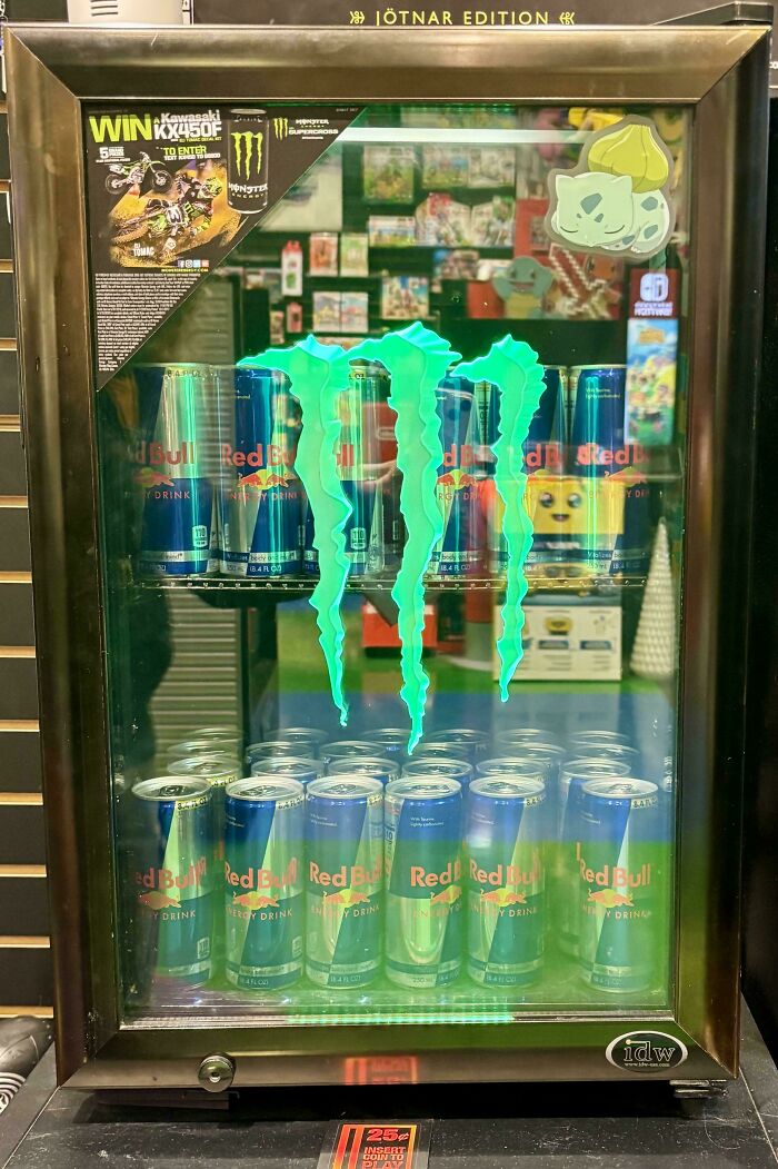Mini fridge with Monster and Red Bull energy drink cans, featuring a glowing Monster logo and promotional stickers.
